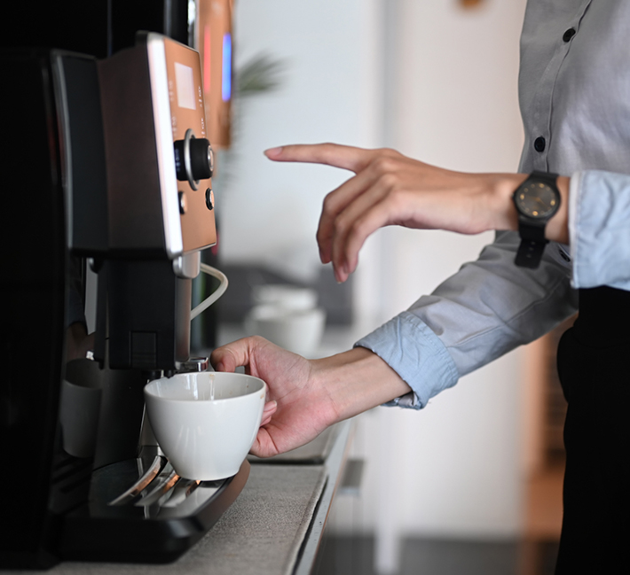 Frau mit Tasse am Kaffeeautomaten